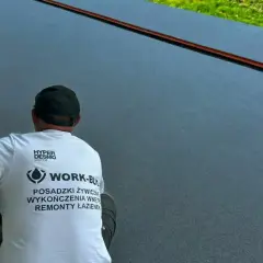Pracownik w czapce i koszulce z logo firmy wykonuje posadzki żywiczne w garażu.