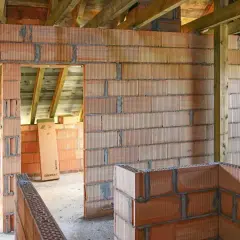 Budowa domu w toku. Widać ściany z pustaków ceramicznych, drewniany strop i elementy konstrukcyjne. Powstaje ścianka kolankowa.