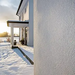 Zimowy krajobraz z domem i szopą. Widoczny źle zatarty tynk na elewacji, który tworzy ciekawą fakturę.