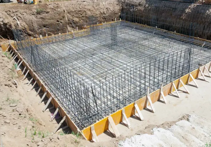 Zbrojenie fundamentów domu w wykopie, otoczone szalunkiem.