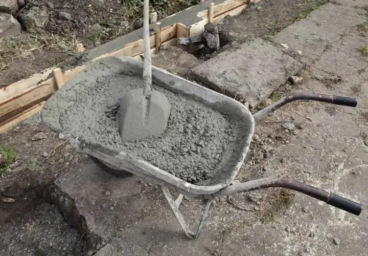 Taczka z betonem i łopatą, gotowa do pracy przy wylewaniu fundamentów. W tle widać szalunki, a całość sugeruje prace budowlane z wykorzystaniem zbrojenia rozproszonego.