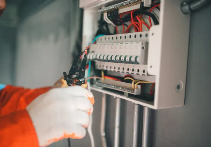 Elektryk w białych rękawicach pracuje przy skrzynce z bezpiecznikami. Zabezpieczenie przedlicznikowe jest kluczowe dla bezpieczeństwa instalacji.