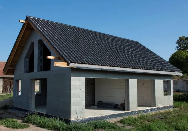 Nowy dom z betonu w stanie surowym, z czarnym dachem i otwartymi przestrzeniami.