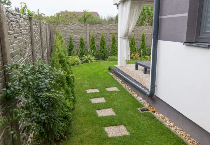 Nowoczesny system odprowadzenia wody z rynien na trawnik, z kamienną ścieżką i zielonym ogrodem.