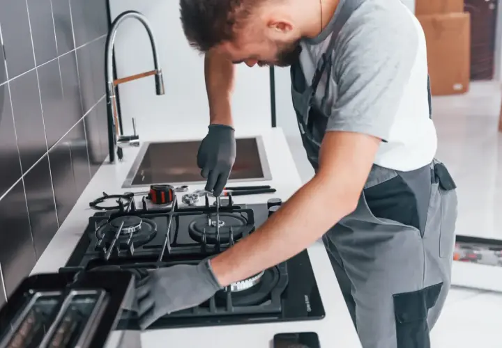 Fachowiec w rękawiczkach dokonuje podłączenia kuchenki gazowej. Narzędzia leżą obok.