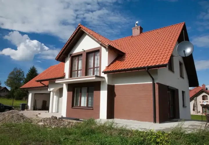 Nowy dom z białymi i brązowymi akcentami na elewacji zewnętrznej, z pomarańczowym dachem.