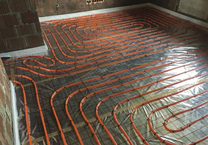 Pomarańczowe rury ogrzewania podłogowego ułożone na folii, przygotowane do wylania betonu. To kluczowy etap hydroizolacji chudziaka.