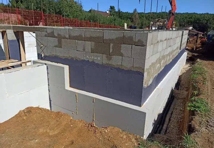 Izolacja fundamentów w starym domu w trakcie prac. Ściany z bloczków betonowych, styropian i hydroizolacja.