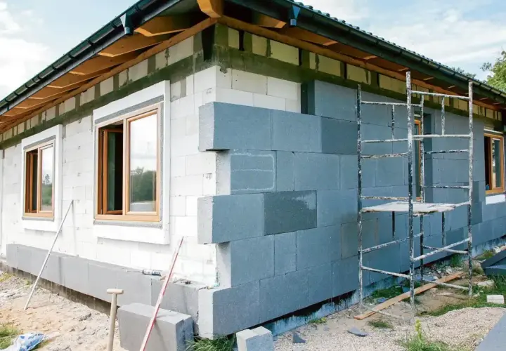 Budowa domu z bloczków betonowych, trwa montaż ścian zewnętrznych. Okna już osadzone, trwa praca nad elewacją.