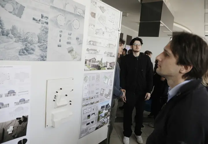 Ludzie oglądają wystawę projektów architektonicznych i makiety budynków.