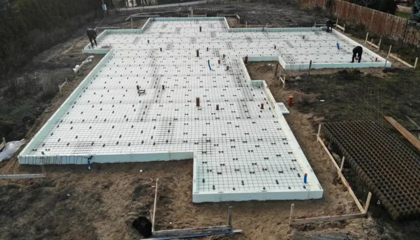 Budowa fundamentów na styropianie, tworząc izolację przed przemarzaniem gruntu. Widać zbrojenie i elementy instalacji.