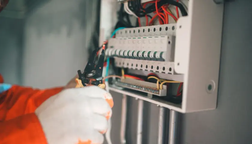 Elektryk w białych rękawicach pracuje przy skrzynce z bezpiecznikami. Zabezpieczenie przedlicznikowe jest kluczowe dla bezpieczeństwa instalacji.