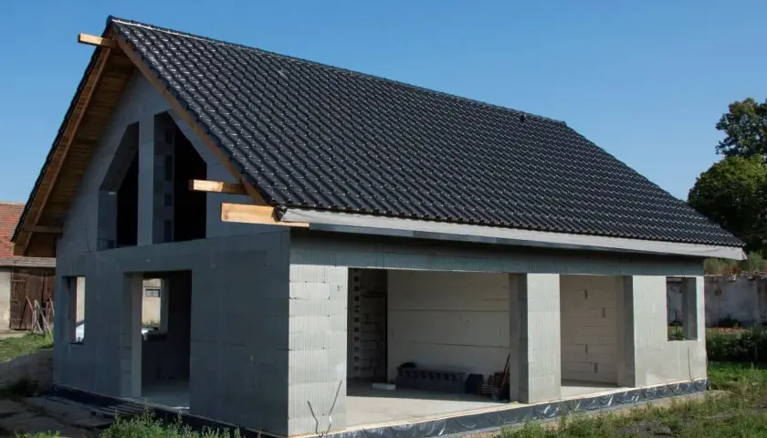 Nowy dom z betonu w stanie surowym, z czarnym dachem i otwartymi przestrzeniami.