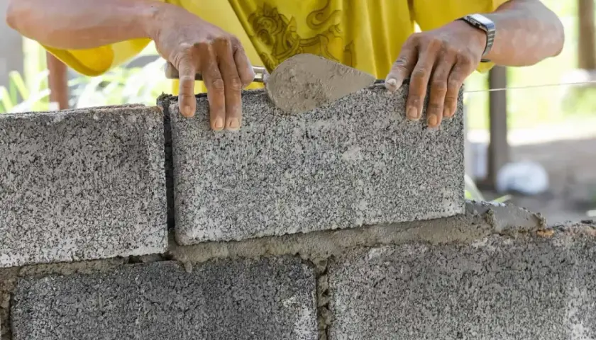Murarz układa betonowy bloczek, sprawdzając jego wymiary.