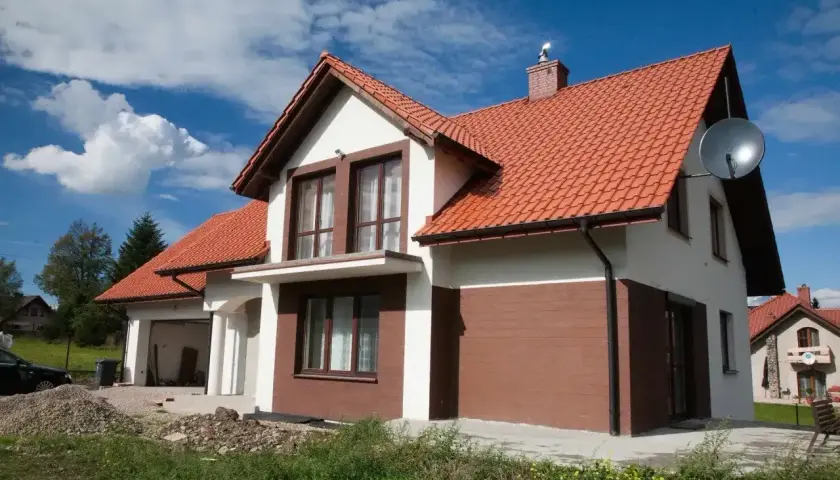 Nowy dom z białymi i brązowymi akcentami na elewacji zewnętrznej, z pomarańczowym dachem.