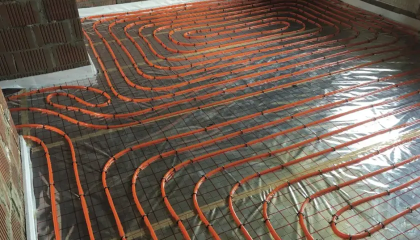 Pomarańczowe rury ogrzewania podłogowego ułożone na folii, przygotowane do wylania betonu. To kluczowy etap hydroizolacji chudziaka.