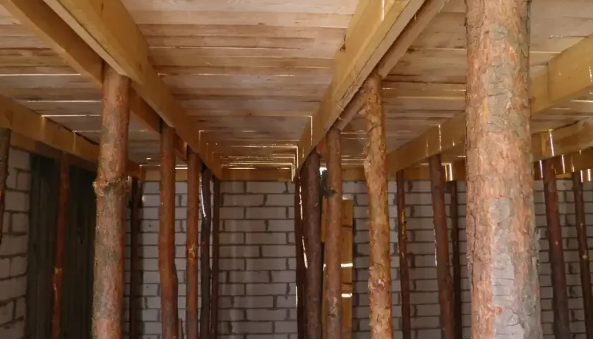 Szalowanie stropu z drewnianych belek i pni drzew, podtrzymujące konstrukcję nad ścianą z pustaków.