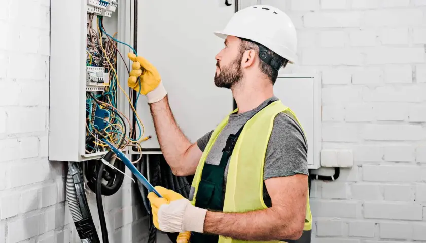 Elektryk w kasku i kamizelce odblaskowej pracuje przy skrzynce z przewodami. Dokładna wycena koszt instalacji elektrycznej wymaga precyzji.