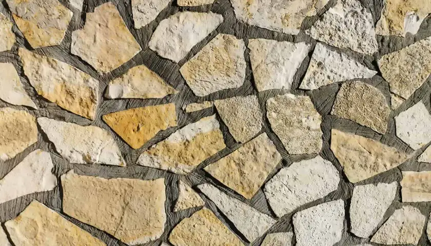 Kamienna ściana z nieregularnych, żółtawych i białych kamieni. Piaskowiec tworzy naturalną, rustykalną mozaikę.