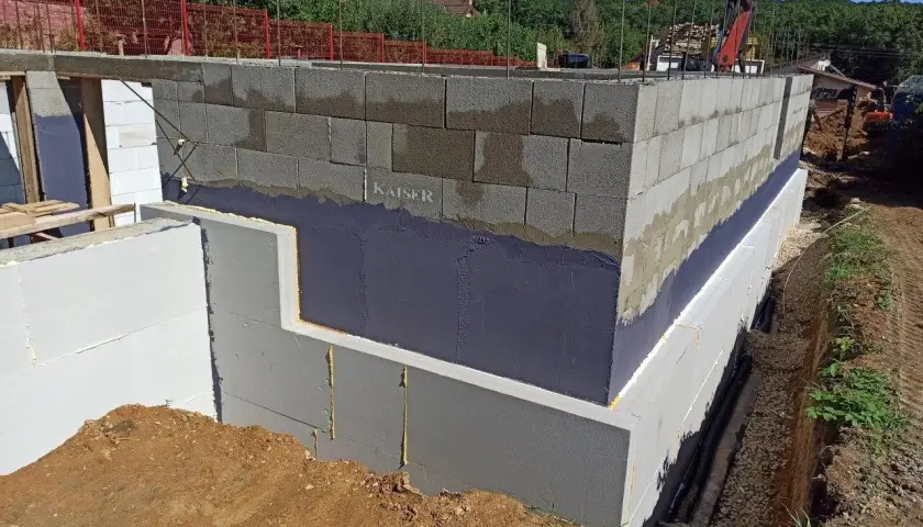 Izolacja fundamentów w starym domu w trakcie prac. Ściany z bloczków betonowych, styropian i hydroizolacja.