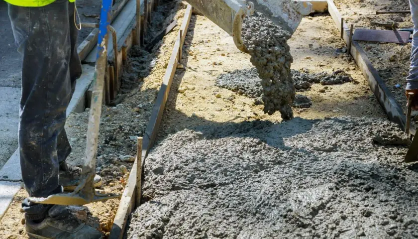 Betoniarka wylewa beton na plac budowy. Pracownik w kamizelce i spodniach przygotowuje teren. Zastanawiasz się, ile kosztuje kubik betonu?