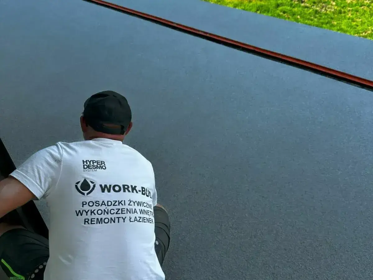 Pracownik w czapce i koszulce z logo firmy wykonuje posadzki żywiczne w garażu.