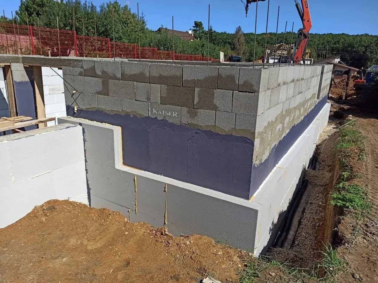 Izolacja fundamentów w starym domu w trakcie prac. Ściany z bloczków betonowych, styropian i hydroizolacja.