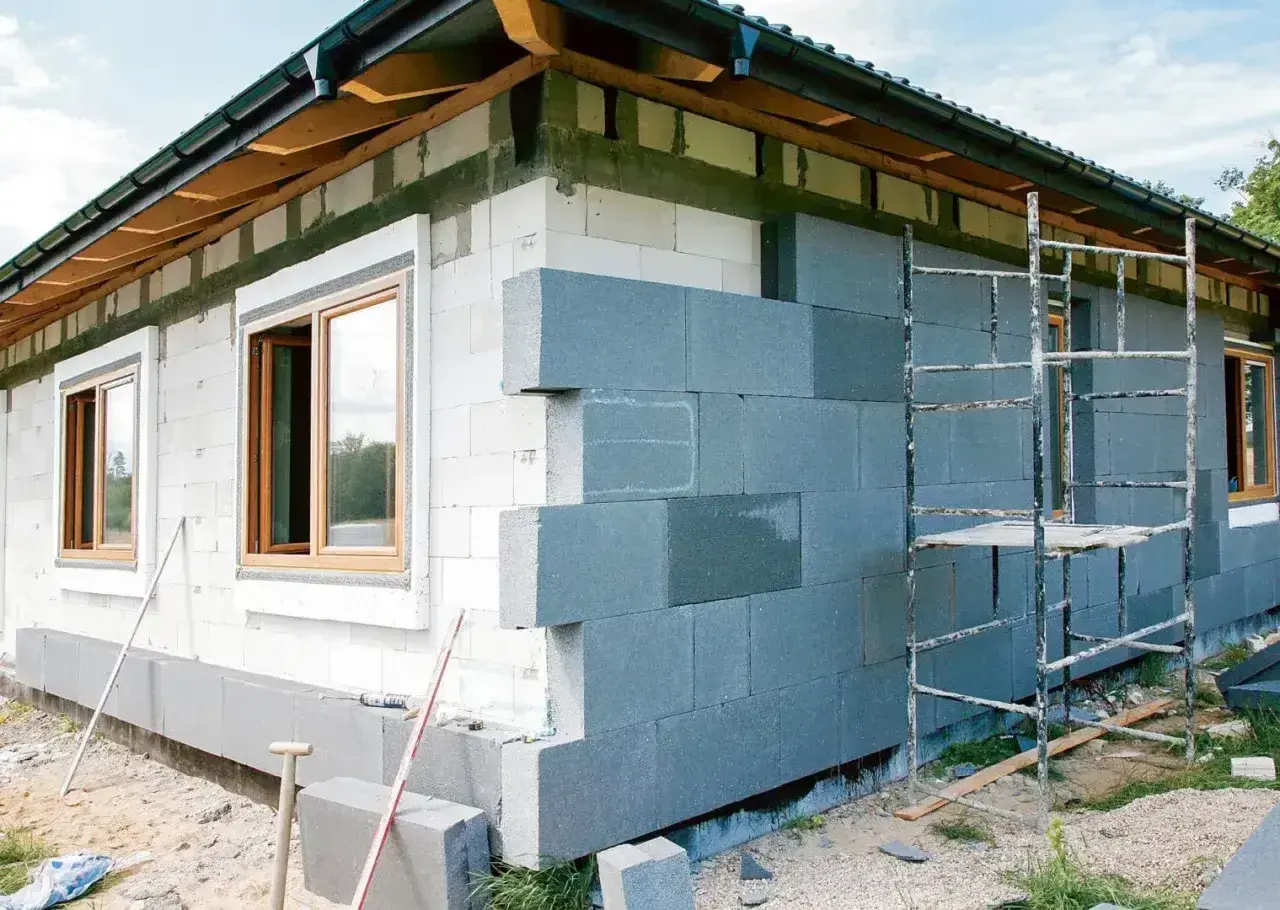 Budowa domu z bloczków betonowych, trwa montaż ścian zewnętrznych. Okna już osadzone, trwa praca nad elewacją.